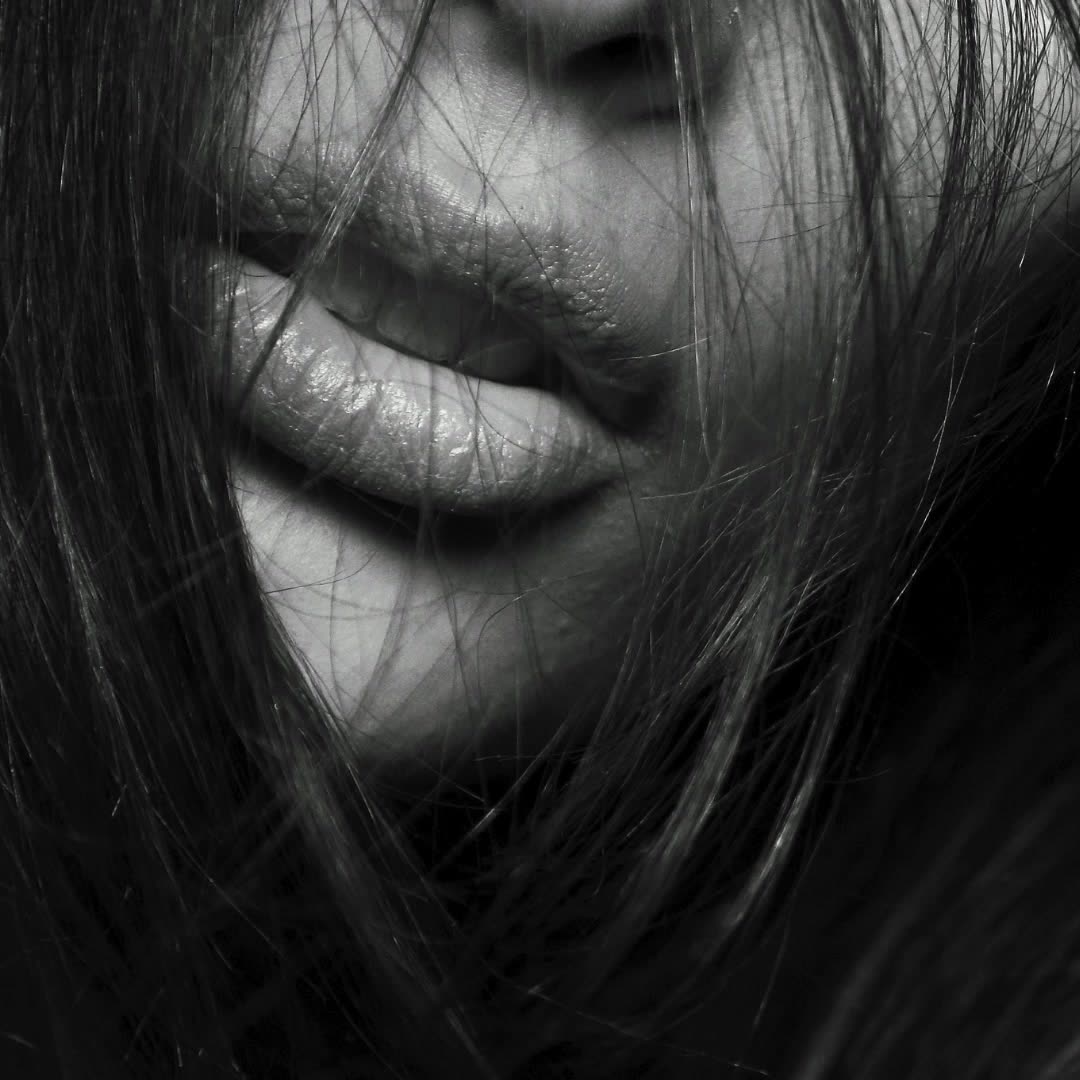 Black-and-white close-up of lips behind strands of hair