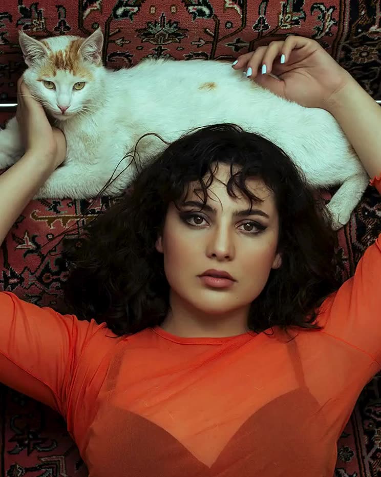 A woman in orange lying on a rug with a white cat